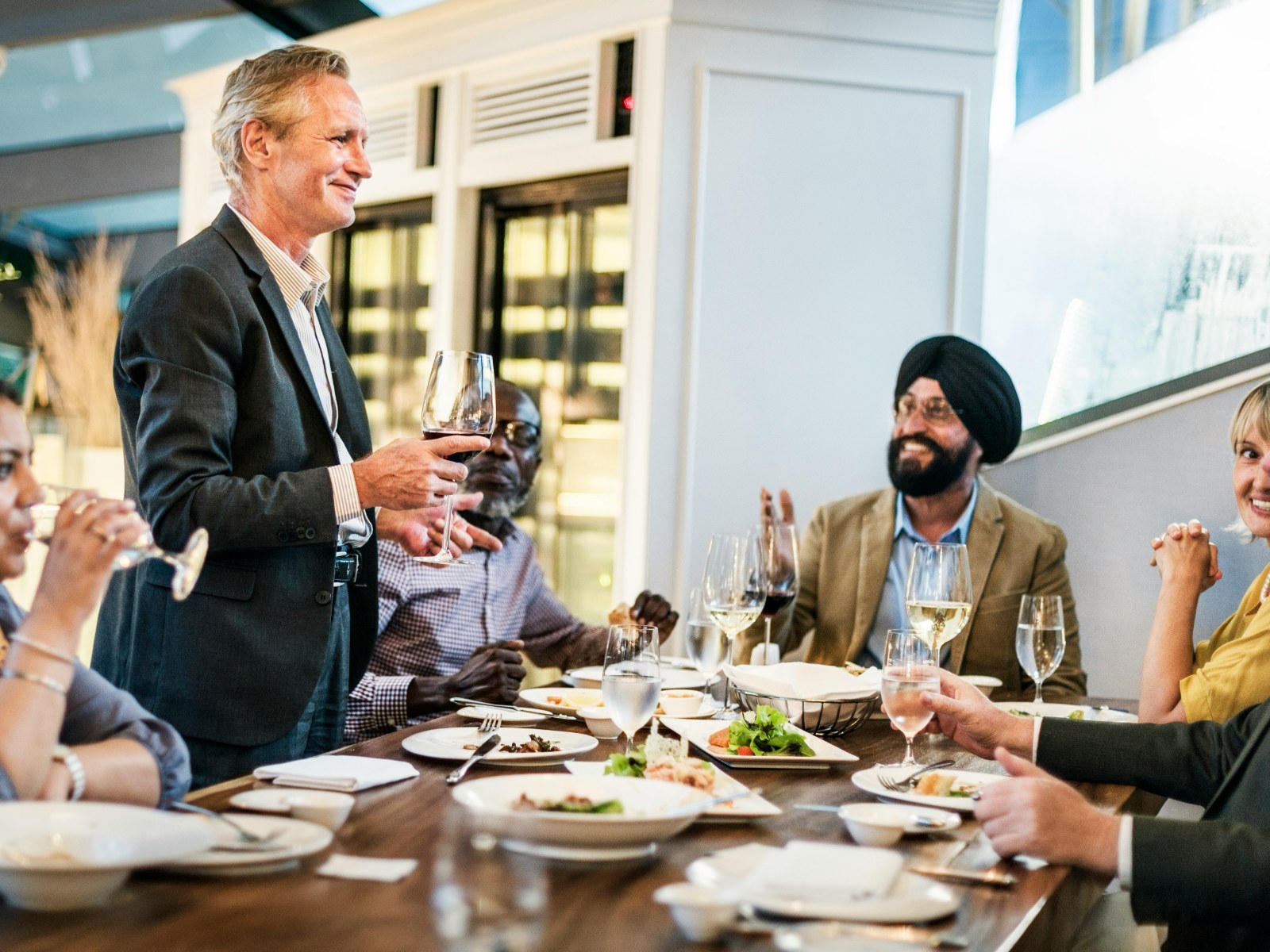 A group of executives round a dinner table, one standing to speak.
